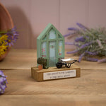 A wooden decorative block featuring a miniature greenhouse with a pair of wellies, a potted tree, and a wheelbarrow on top, with a plaque that says 'Time spent in the garden is time well spent'.