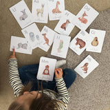 A child is playing with a set of white animal-themed alphabet flashcards with a letter on each card, featuring illustrations of various animals such as a giraffe, a zebra, a deer, and a bear.