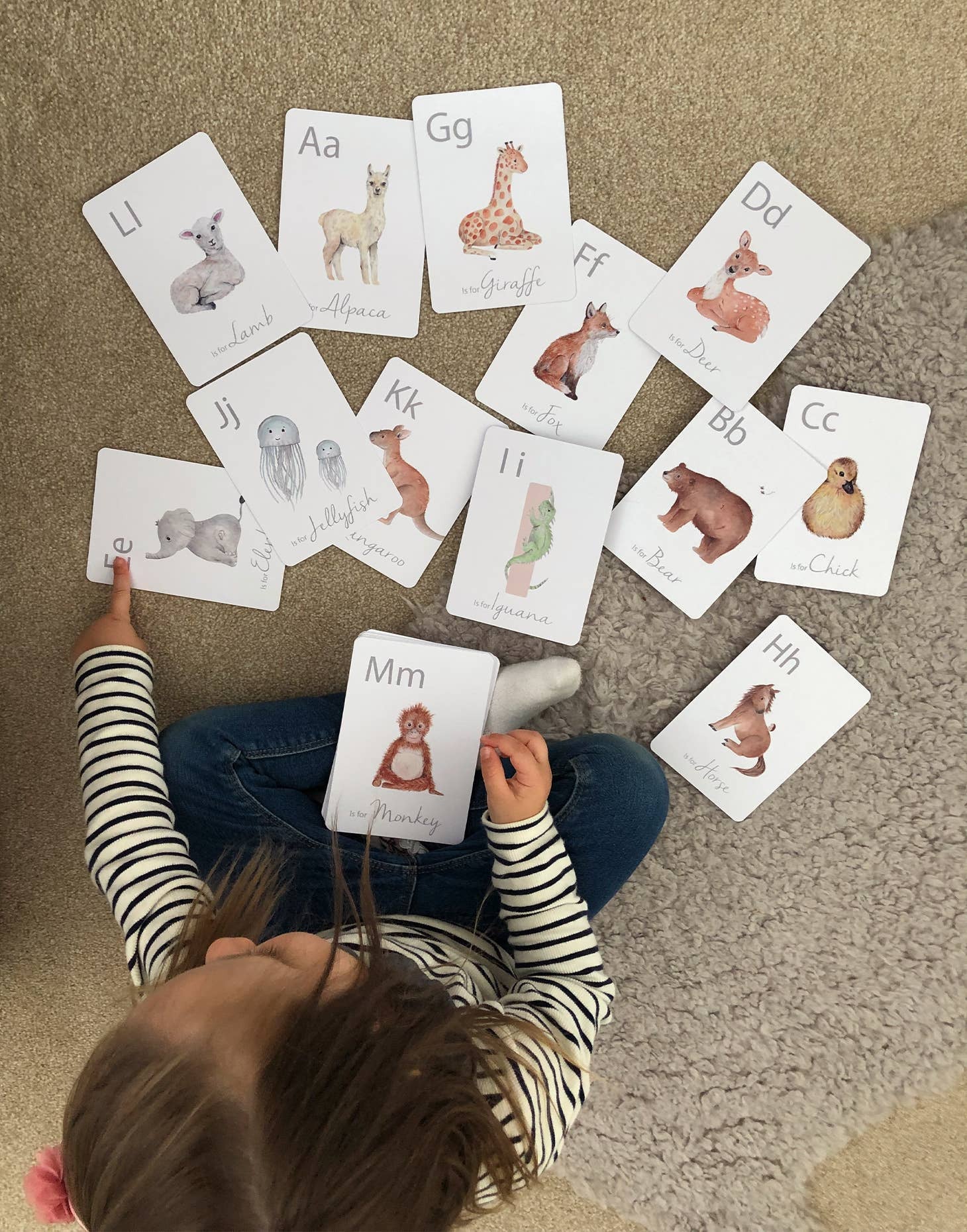 A child is playing with a set of white animal-themed alphabet flashcards with a letter on each card, featuring illustrations of various animals such as a giraffe, a zebra, a deer, and a bear.
