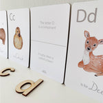 A child is playing with a set of white animal-themed alphabet flashcards with a letter on each card, featuring illustrations of various animals such as a giraffe, a zebra, a deer, and a bear.