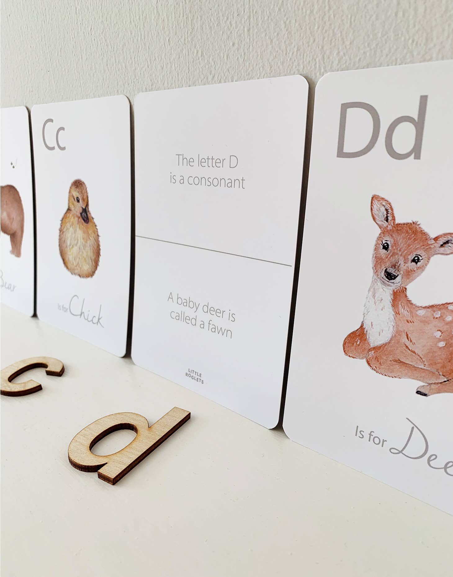 A child is playing with a set of white animal-themed alphabet flashcards with a letter on each card, featuring illustrations of various animals such as a giraffe, a zebra, a deer, and a bear.