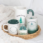 Set of mugs and a candle with 'Farm Fresh' and 'Winter Wonderland' text on a textured surface.