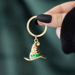 Gold and green keychain shaped like a witch's hat held by a hand against a dark background