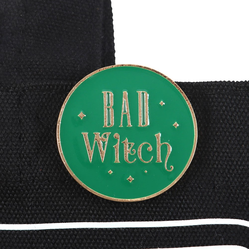 Green enamel pin with 'Bad Witch' text on a black background