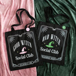 Two black tote bags with 'Good Witch Social Club' and 'Bad Witch Social Club' text on a pink and green fabric background.