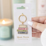 Book-themed keychain on packaging with a blurred candle in the background