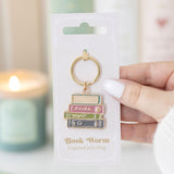 Book-themed keychain on packaging with a blurred candle in the background