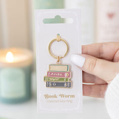 Book-themed keychain on packaging with a blurred candle in the background