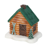 Miniature log cabin with green roof, skis, and a small tree on a white background