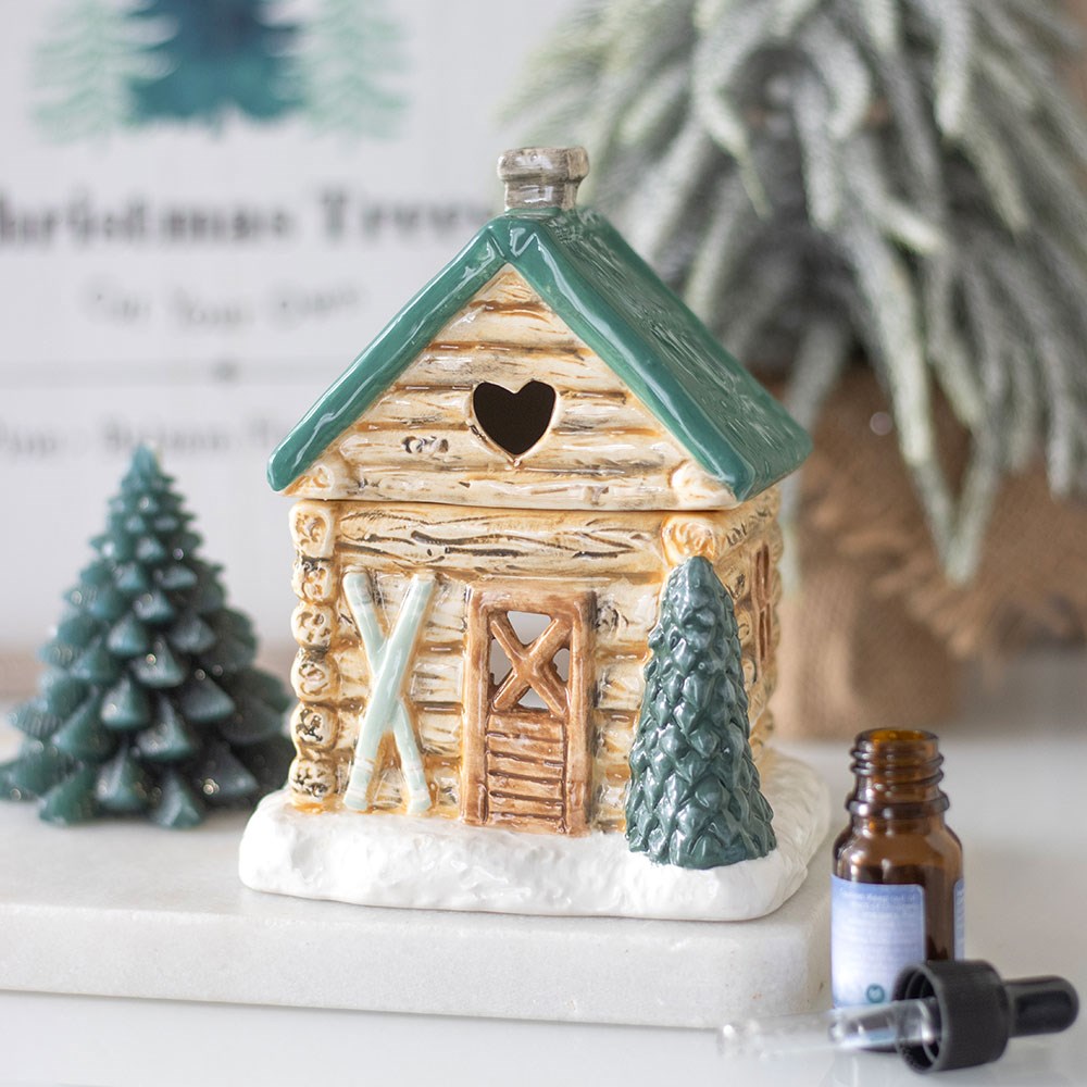 Decorative log cabin with a heart-shaped window, surrounded by small trees and an essential oil bottle.