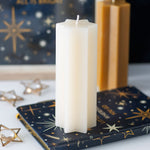 White candle on a decorative book with gold stars and text, against a dark background.