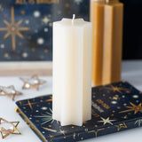 White candle on a decorative book with gold stars and text, against a dark background.