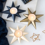 Star-shaped candle holders in black, gold, and white on a light background