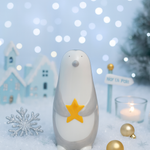 Decorative penguin with a star on a snowy background with lights and small houses.