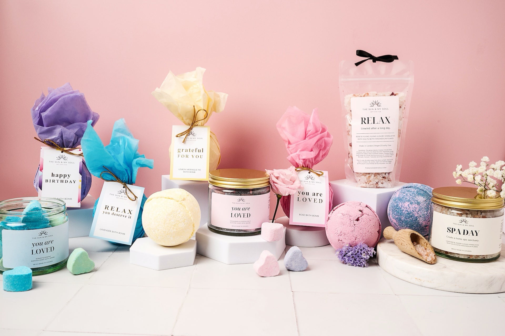 Collection of bath bombs, candles, and other spa products on a pink background