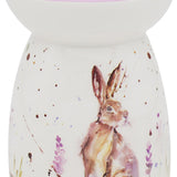 A ceramic wax burner with a hand-painted design featuring a hare, lavender flowers, and a purple field.