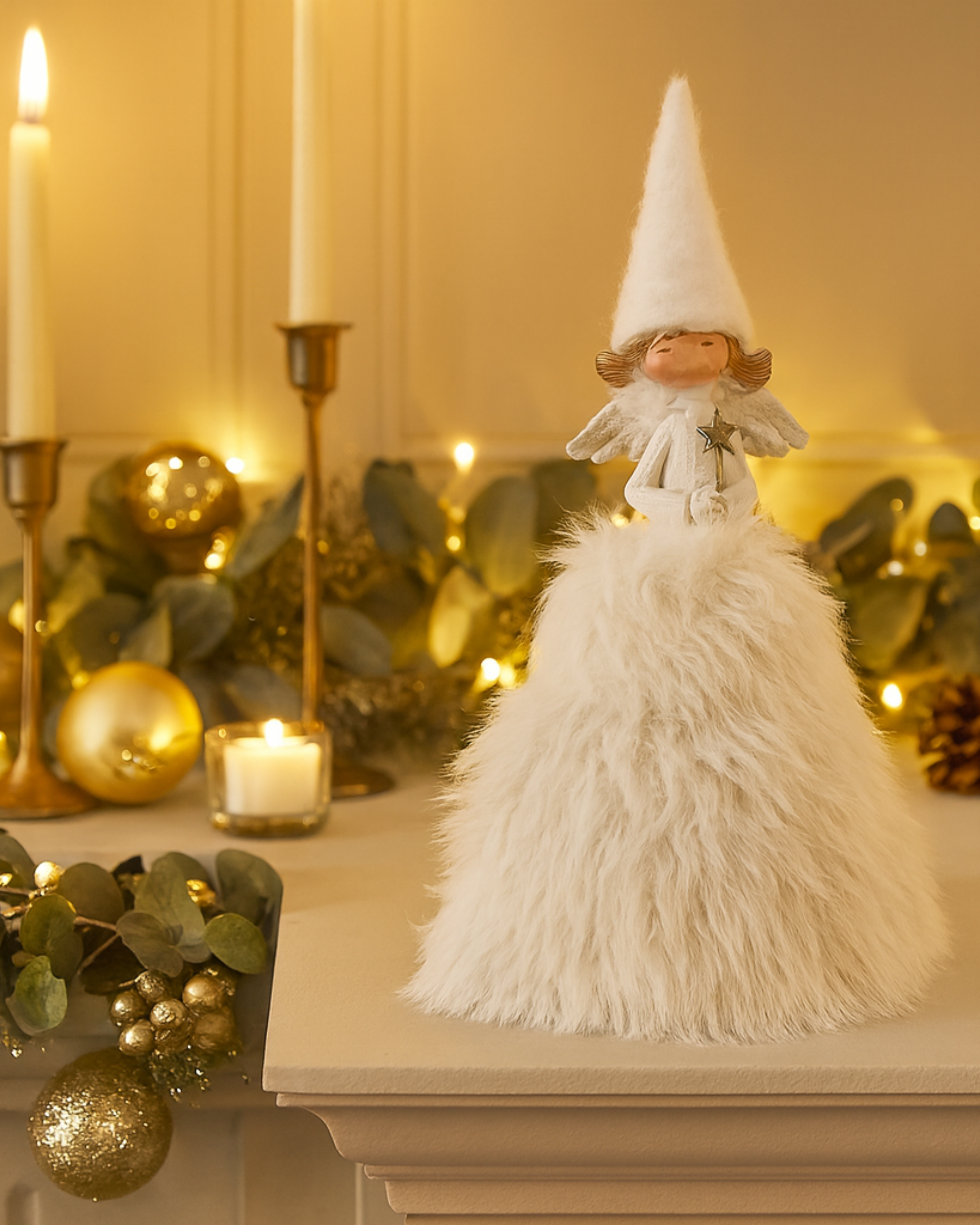 Decorative angel figure on a mantelpiece with candles and ornaments