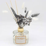 A grey pampas reed diffuser with dried plants and sticks, housed in a clear glass bottle with a label reading 'Desire'.