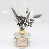A grey pampas reed diffuser with dried plants and sticks, housed in a clear glass bottle with a label reading 'Desire'.