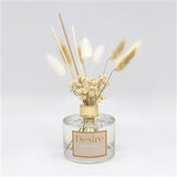 A clear glass reed diffuser with a gold-colored lid and natural pampas reeds. The label 'desire' is visible on the glass.