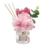 An artificial hydrangea diffuser with a clear bottle and pink flowers, accompanied by wooden sticks and decorative leaves.