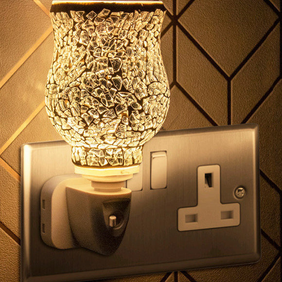 A silver mosaic plug-in warmer with a UK plug, mounted on a wall, emitting a glow.