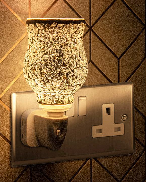A silver mosaic plug-in warmer with a UK plug, mounted on a wall, emitting a glow.