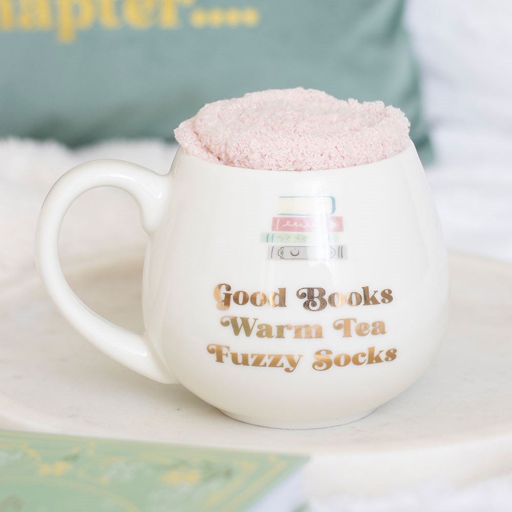 White mug with text 'Good Books Warm Tea Fuzzy Socks' on a white surface.