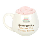 White mug with pink fuzzy ball inside, featuring text 'Good Books Warm Tea Fuzzy Socks' on a white background.