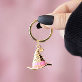 Gold and pink witch's hat keychain held by a hand against a pink background
