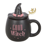 Black mug with witch hat lid, pink 'Good Witch' text, and gold moon and star decoration on a white background.