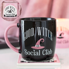 Black mug with 'Good Witch Social Club' text and pink witch hat design on a pink coaster.