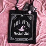 Black tote bag with 'Good Witch Social Club' design on a pink fabric background