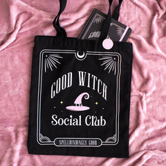 Black tote bag with 'Good Witch Social Club' design on a pink fabric background