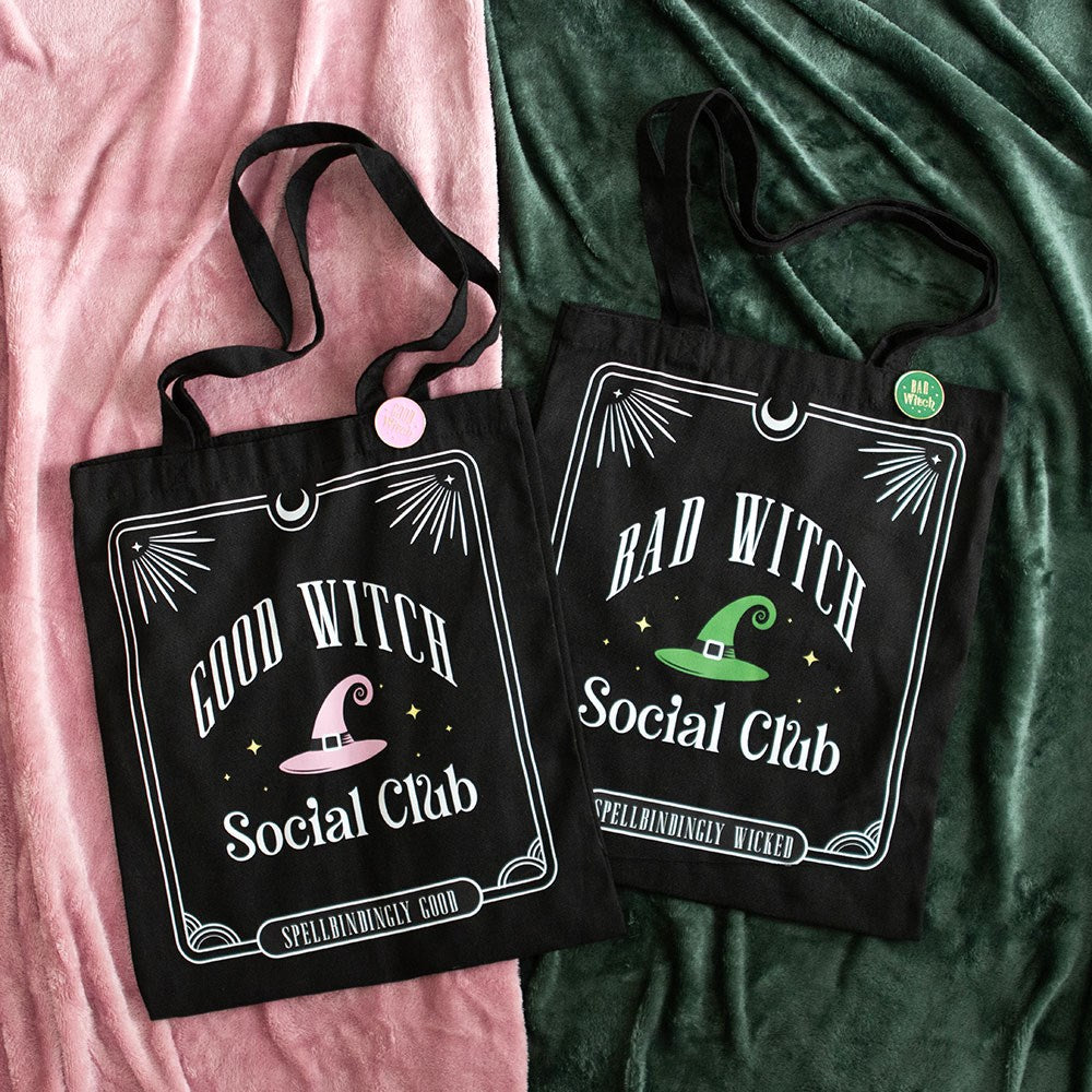 Two black tote bags with witch-themed designs on a pink and green fabric background.