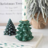 Green tree-shaped candle holder with a white candle featuring green trees on a white surface.