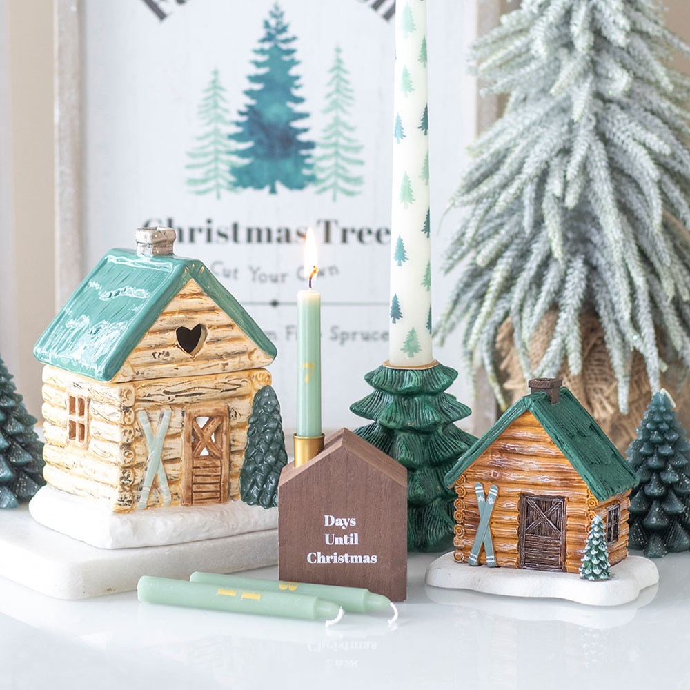 Decorative Christmas scene with log cabin candle holders, candles, and a small house timer.