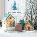 Decorative Christmas scene with log cabin candle holders, candles, and a small house timer.
