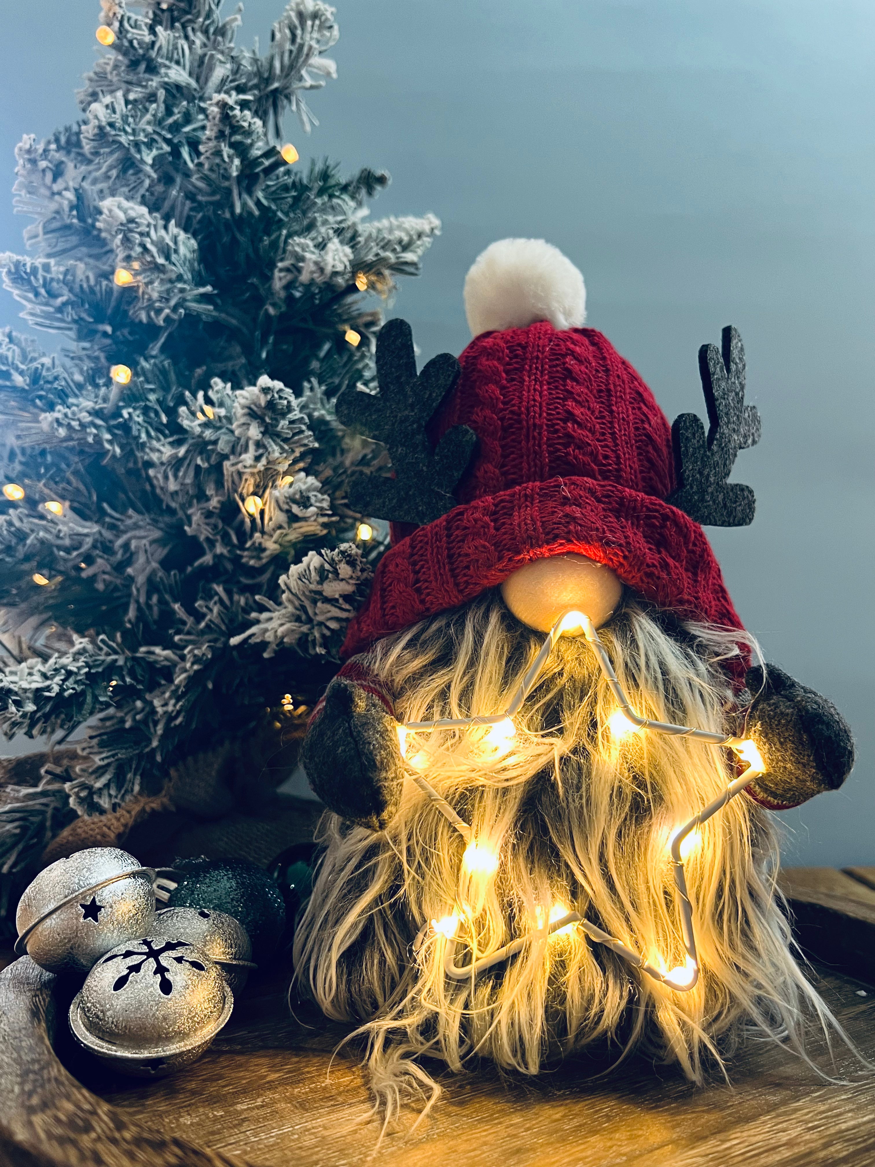 A whimsical figurine of a gonk with a red knitted hat and a fluffy pom-pom, featuring an LED star on its head.