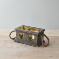 A grey wooden candle holder tray with heart cut-out details and rope handles, placed on a wooden surface.