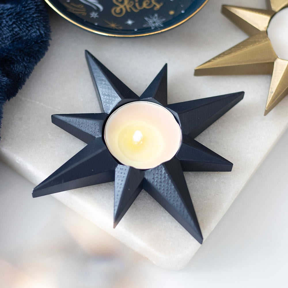 Black star-shaped candle holder with a lit candle on a light surface.