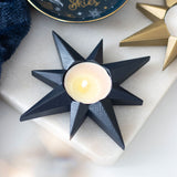 Black star-shaped candle holder with a lit candle on a light surface.