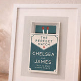 Framed print with 'The Perfect Match' text on a wooden surface with a candle and vase in the background.