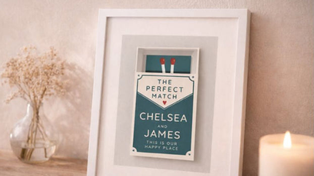 Framed print with 'The Perfect Match' text on a wooden surface with a candle and vase in the background.