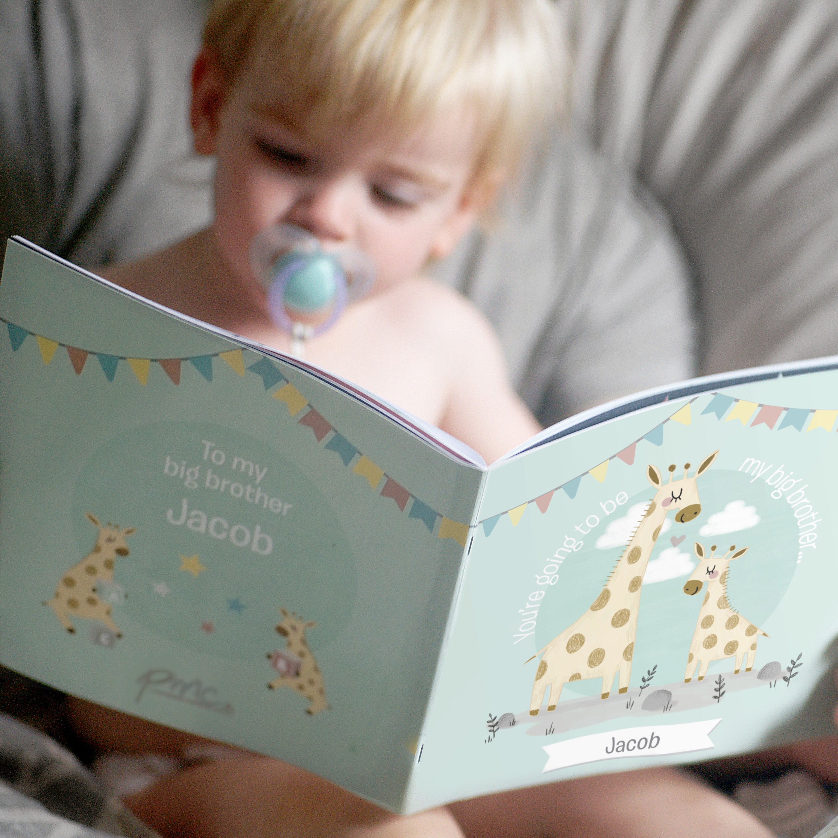 A personalised storybook with a blue cover, featuring illustrations of giraffes and text that includes the name 'William'. A man is reading the book to a child.