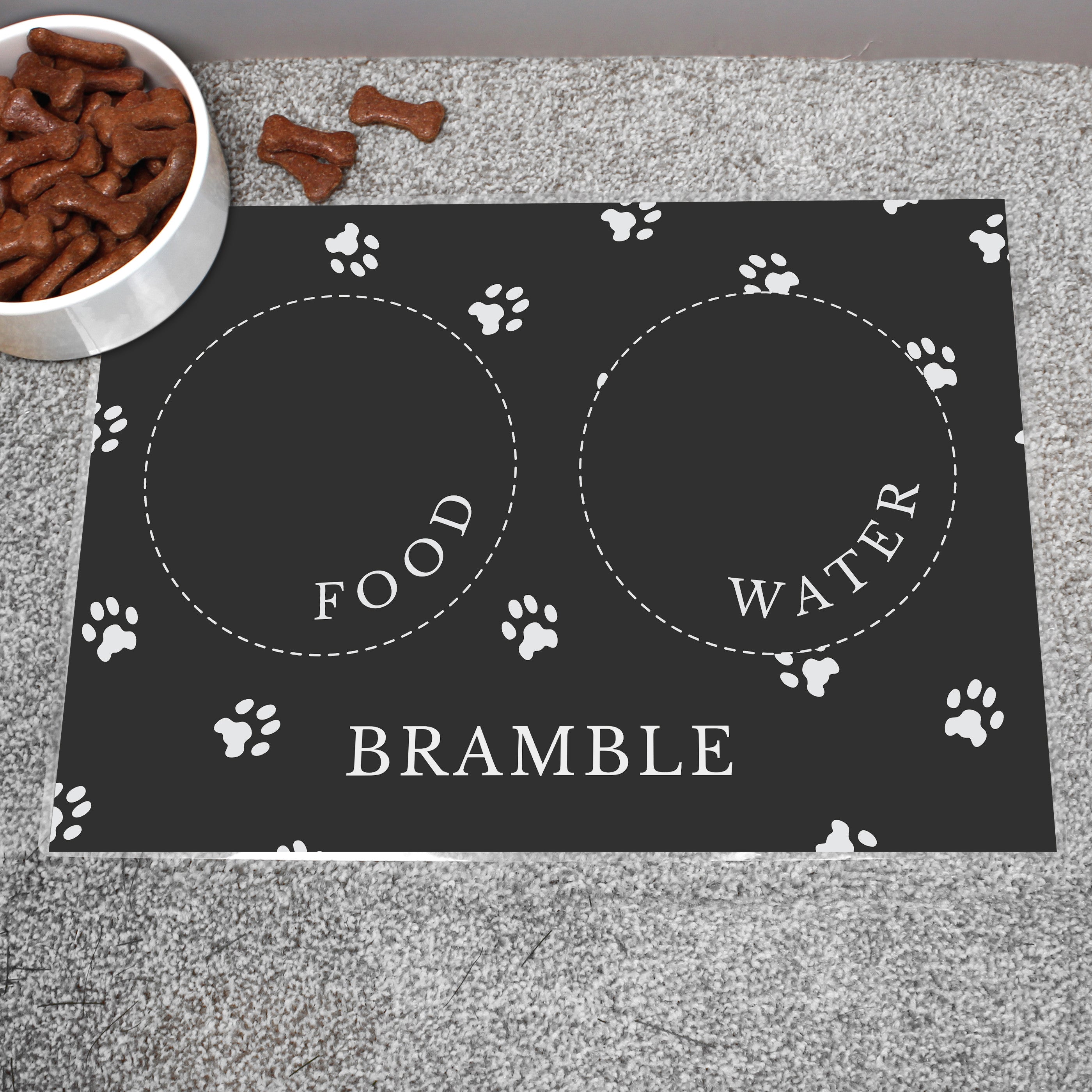Black personalised pet bowl mat, with a bowl full of dog treats to the side 