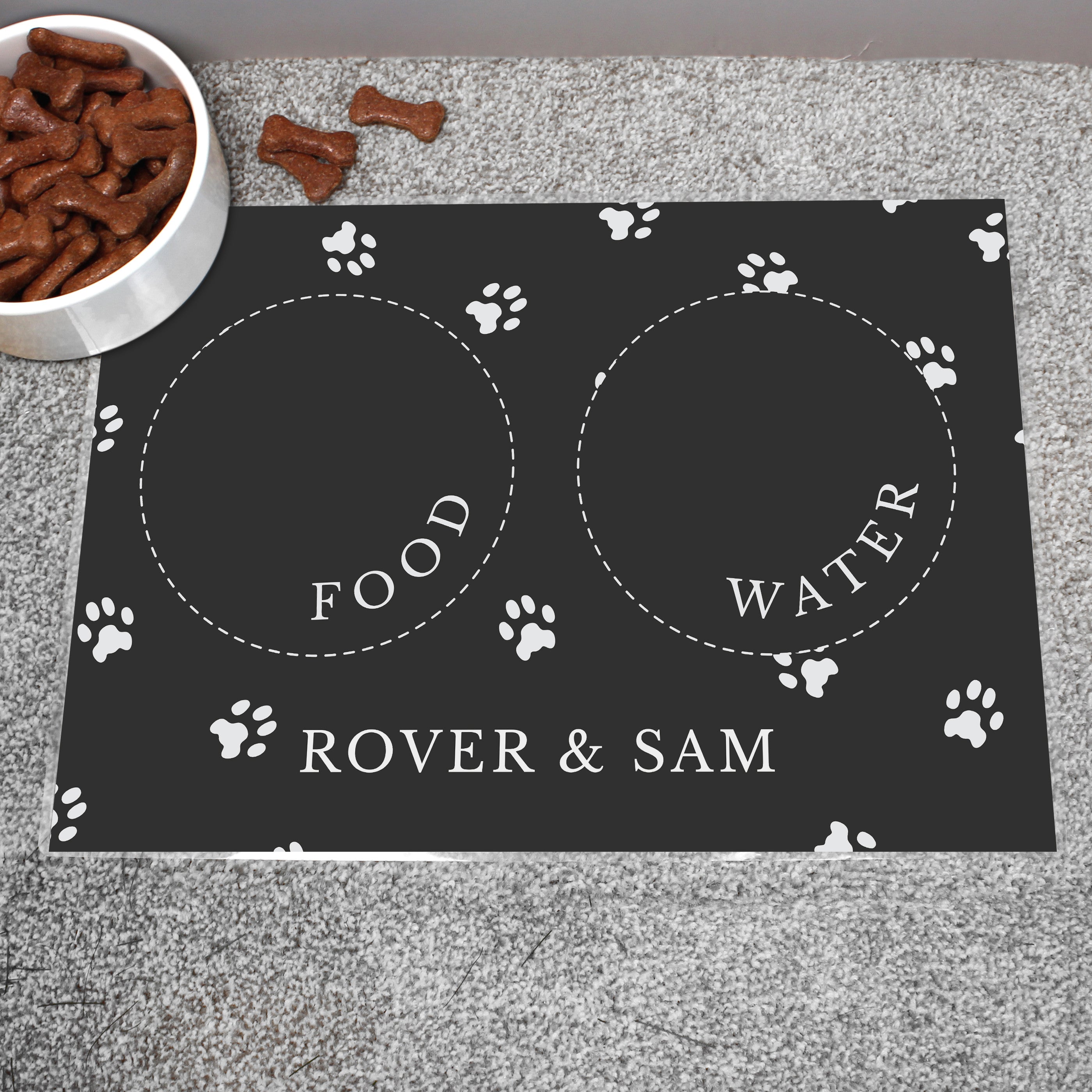 Black personalised pet bowl mat, with a bowl full of dog treats to the side 