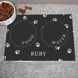 Black personalised pet bowl mat, with a bowl full of dog treats to the side 