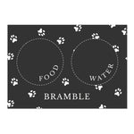 Black personalised pet bowl mat, with a bowl full of dog treats to the side 