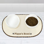 A beige microfibre pet bowl mat with a brown paw print design, personalised with the name 'Pippa', alongside two white bowls filled with pet food.